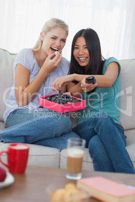 Friends laughing at tv and sharing box of chocolates