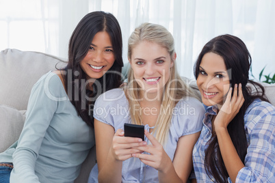 Smiling friends holding smartphone looking at camera