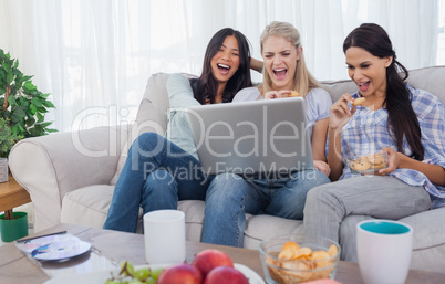 Smiling friends looking at laptop together and eating cookies
