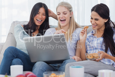 Laughing friends looking at laptop together and eating cookies