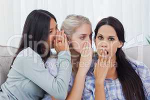 Two friends whispering secret to shocked brunette