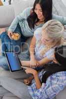 Smiling friends using digital tablet together and eating cookies