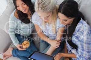 Laughing friends using digital tablet together and eating cookie