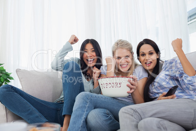 Friends cheering at television with bowl of popcorn