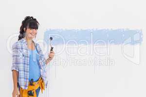 Woman painting wall blue and smiling at camera