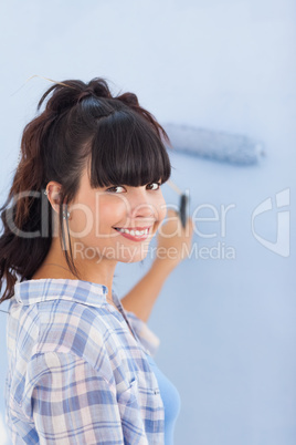 Cute woman painting wall blue and smiling at camera