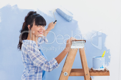 Woman using paint roller to paint wall and smiling at camera