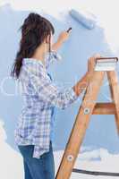 Woman using paint roller to paint wall blue