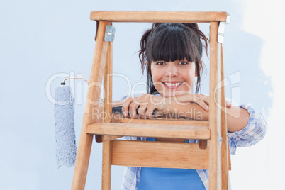 Smiling woman holding paint roller leaning on ladder