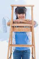 Happy woman holding paint roller leaning on ladder