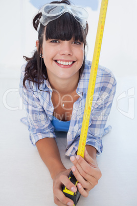 Happy woman lying on floor with measuring tape and safety goggle