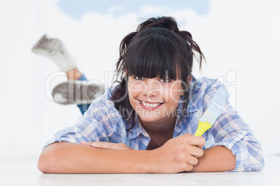 Happy woman lying on floor holding paint brush