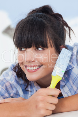 Cute woman lying on floor holding paint brush