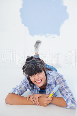 Brunette woman lying on floor holding paint brush