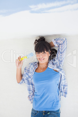 Attractive woman lying on floor holding paint brush overhead