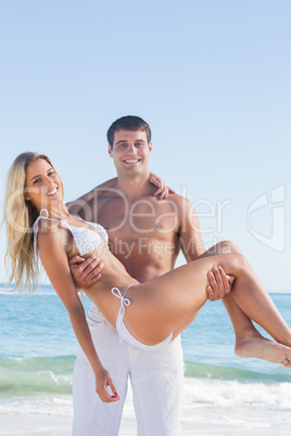 Strong man carrying his pretty girlfriend smiling at camera