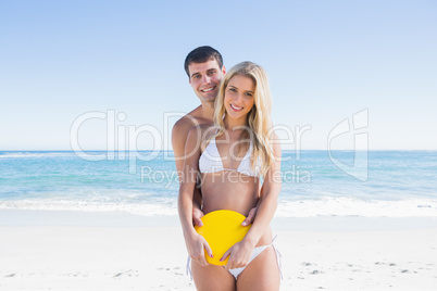 Man holding frisbee and embracing his girlfriend smiling at came