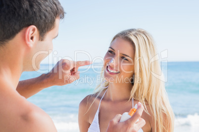 Man putting sun cream on smiling girlfriends nose