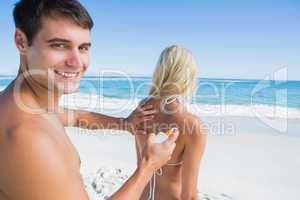 Man putting sun cream on girlfriends back smiling at camera