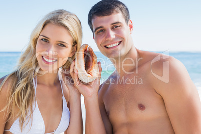 Happy couple listening to seashell smiling at camera