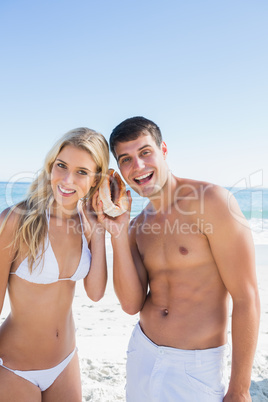 Attractive couple listening to seashell smiling at camera