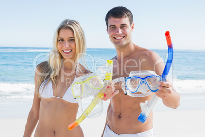 Attractive couple showing snorkels and goggles to camera