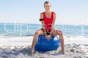 Fit young blonde sitting on exercise ball smiling at camera