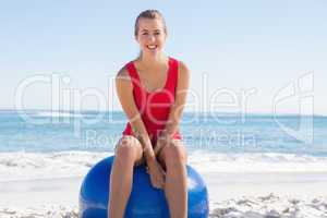 Fit young woman sitting on exercise ball smiling at camera