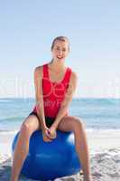 Fit happy woman sitting on exercise ball looking at camera