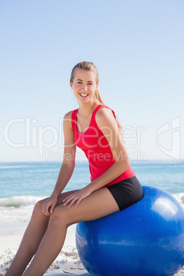 Athletic young blonde sitting on exercise ball looking at camera