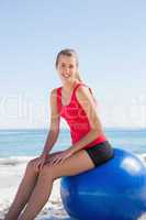Athletic young blonde sitting on exercise ball looking at camera