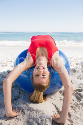 Fit blonde stretching back on exercise ball smiling at camera