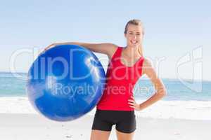 Fit blonde holding exercise ball smiling at camera