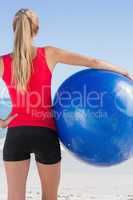 Fit blonde holding exercise ball looking at ocean