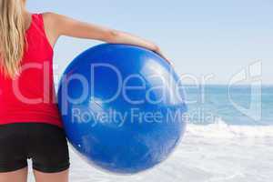 Fit blonde holding exercise ball looking at waves