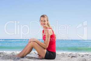 Fit blonde sitting on sand smiling at camera