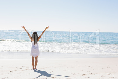 Brunette in white sun dress standing by the water with arms rais