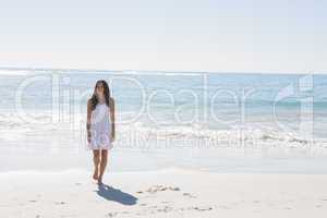 Brunette in white sun dress walking from the sea