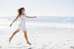 Happy brunette in white sun dress skipping on the sand