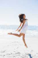 Happy brunette in white sun dress dancing on the sand