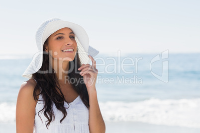 Beautiful brunette in white sunhat looking away and touching hat