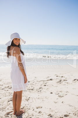 Brunette in white sunhat and dress looking over her shoulder at