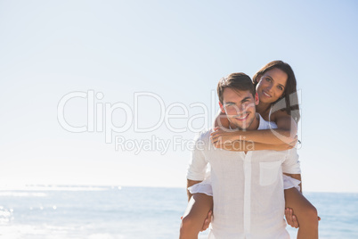 Smiling man giving girlfriend a piggy back looking at camera