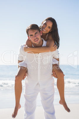 Smiling man giving happy girlfriend a piggy back looking at came