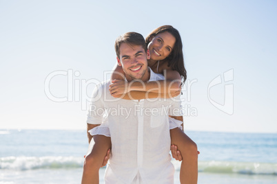 Handsome man giving girlfriend a piggy back smiling at camera