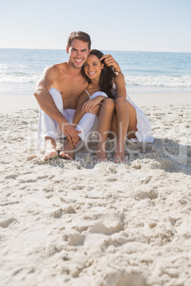 Cuddling couple smiling at camera sitting on sand