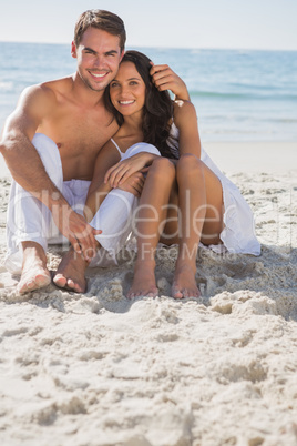 Embracing couple smiling at camera sitting on sand