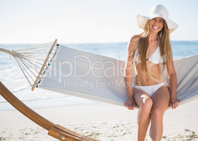 Pretty blonde wearing bikini and sunhat sitting on hammock and s