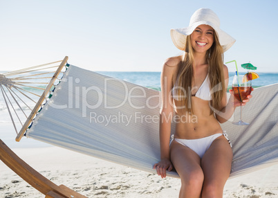 Pretty blonde wearing bikini and sunhat sitting on hammock with