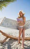 Cheerful blonde sitting on hammock reading book